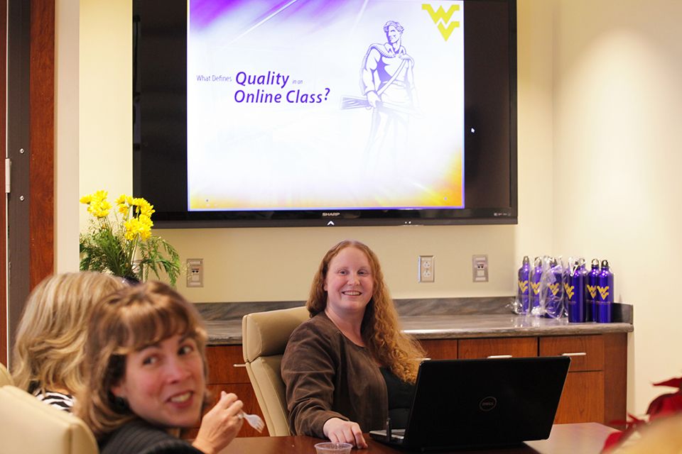 Tracey Beckley and Erin Kelley face the camera, in front of a screen with 'What Defines Quality in an Online Class?' displayed on it.